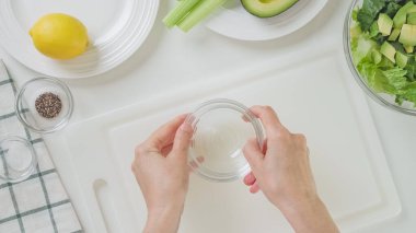 Yeşil salata tarifi. Kadın salata sosu yapıyor. İçindekiler beyaz arkaplan üzerine yakın plan, düz yatar