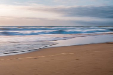 Sahilde gün batımı. Soyut deniz manzarası, yumuşak bulanık deniz, kumsal ve gün batımında bulutlu gökyüzü.