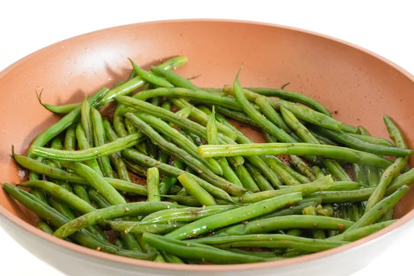 French green beans (Haricots Verts) close-up on frying pan with salt and garlic seasoning, white background