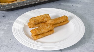 Balık, mutfak masasındaki beyaz tabakta çıtır çıtır altın bir ekmeğe yapışır.