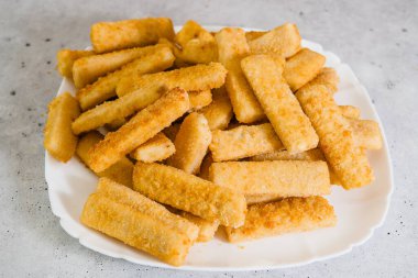 Vahşi hayvanlardan yapılan gevrek ekmekli balık çubukları Alaska Pollock 'unu açık gri arka planda beyaz plakaya yakın plan çekerken yakalamış.