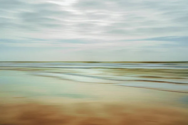 Light abstract seascape. Sand beach at sunset, cloudy sky in the background, motion blur
