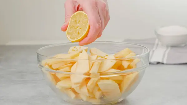 Apple slices in a glass bowl. Topping slices with lemon juice. Apple cake recipe, woman hands