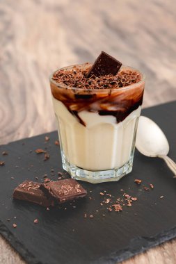Siyah çikolata soslu beyaz çikolatalı vanilyalı puding. Servis masasındaki bardakta mükemmel lezzetli bir tatlı.