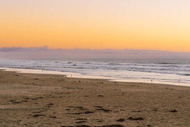 Sahilde nefes kesen bir gün batımı, göğü sarının çarpıcı tonlarıyla boyar. Huzurlu sahnenin üzerine ılık ve dingin bir ışık saçar.