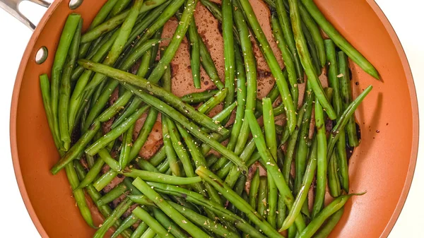 Pan fried French green beans (Haricots Verts) recipe. String beans on a frying pan with soy sauce, and Italian seasoning, close-up view from above