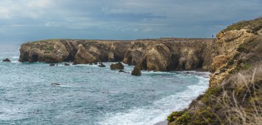 Engebeli kayalıkları ve çarpan dalgalarıyla kıyı manzarasının dramatik güzelliğini gösteren nefes kesici bir manzara. Montana de Oro, Kaliforniya