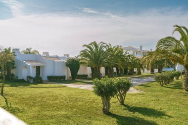 Palmiye ağaçlarıyla çevrili canlı turistik bir tatil beldesinde lüks tatilleri simgeleyen bir dizi apartman dairesi. Parlak güneşli bir gün, açık mavi bir gökyüzü.