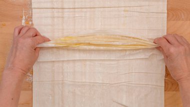 Krem peynirli hamur tatlısı. Kadın elleri tereyağlı hamur katmanlarını, yakın çekim pişirme sürecini, düz uzanma, ahşap arka plan