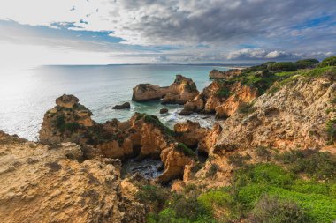 Algarve, Portekiz 'deki Rocky kıyı şeridi ve arka planda dramatik bulutlu gökyüzü