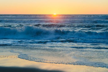 Deniz dalgaları batan güneşin sıcacık, ruhani ışığı altında parlar, ufku nefes kesen ateşli portakallar ve yumuşak maviler ile boyarlar, sakin bir sahne, kopyalama alanı.