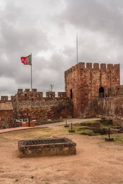 Yeşillik Silves Kalesi 'nin kasvetli gökyüzünün altındaki mazgallı siperlerini kuşatır. Silves, Portekiz, 3 Ocak 2024