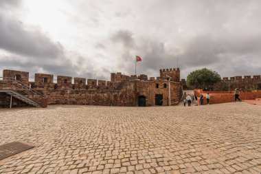 Ziyaretçiler bulutlu bir gökyüzünün altındaki tarihi Silves Şatosu 'nun geniş avlusunu keşfediyorlar. Silves, Portekiz, 3 Ocak 2024