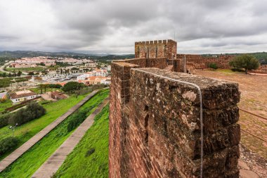 The robust red walls of Silves Castle, with a visitor enjoying the view from the ramparts. Silves, Portugal, January 3, 2024 clipart