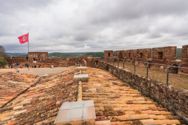Silves Kalesi 'nin terasotta döşemeli çatılarında Portekiz bayrağı var, geniş bir manzaraya bakıyor. Silves, Portekiz, 3 Ocak 2024
