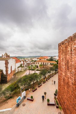 Visitors walk along the ramparts and ruins of Silves Castle under a waving Portuguese flag. Silves, Portugal, January 3, 2024 clipart