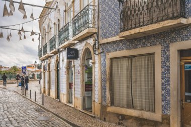 Tavira, Portekiz, 8 Ocak 2024. Portekiz, Tavira 'da bir kaldırım taşı caddesi. Önü karmaşık mavi ve beyaz fayanslar ve demir balkonlarla süslenmiş bir bina..