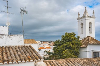 Tavira, Portekiz 'deki çatı manzarası, bir kilise kulesi ve uydu antenleri, gelenek ve modernliğin bir karışımını gösteriyor..