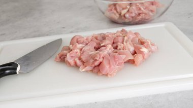 Doğranmış çiğ tavuk filetosu mutfak masasındaki beyaz plastik kesim tahtasının üzerinde.