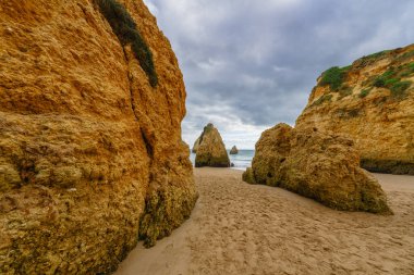 Dağılmış kayalar, kumlu bir sahil ve bulutlu bir gökyüzü ile engebeli bir sahil. Algarve sahili, Portekiz