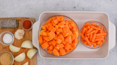 Kızarmış tereyağlı kabak çorbası tarifi. Soyulmuş ve çekirdeksiz kabak küpleri, havuç, soğan, sarımsak ve baharatlar mutfak masasındaki seramik fırın kabında yakın plan.