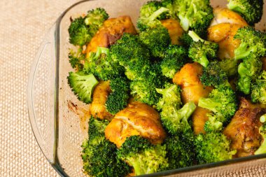 Fırından yeni çıkmış, cam bir kabın içinde tavuk budu ve brokoli. Mutfak masasının üstünde yakın plan bir yemek.