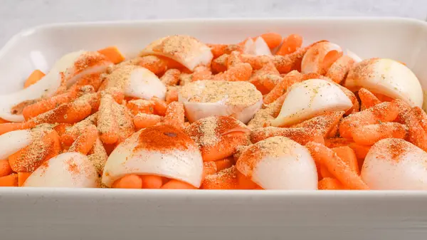 stock image Roasted butternut squash soup recipe. Peeled and seedless squash cubes, carrot, onion, garlic, and spices close-up in a ceramic baking dish on the kitchen table