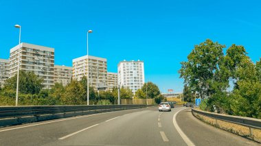 Lizbon, Portekiz, 3 Ağustos 2024. Arabalar arka planda yüksek katlı apartmanlar ve yeşillikler olan bir yol boyunca gidiyor..