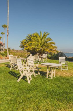 Beyaz sandalyeli ve masalı açık hava oturma alanı bir tatil köyünün önündeki çimenli çimenlikte..