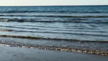 Açık deniz dalgaları, parlak bir gökyüzünün altındaki kumlu bir plaja nazikçe sokulur. Yüksek kalite 4k görüntü
