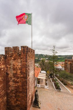Ziyaretçiler, Portekiz bayrağı dalgalanan Silves Kalesi 'nin surları ve harabeleri boyunca yürüyorlar. Silves, Portekiz, 3 Ocak 2024.
