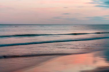 Sakin okyanus dalgalarına karışan yumuşak pastel günbatımı.