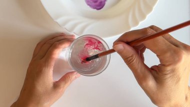 Boya fırçası, berrak bir bardak suda pembe bir suluboya, yakın görüş.