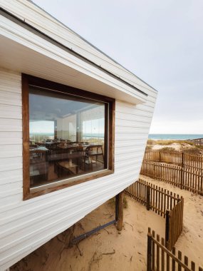 Okyanus ve kumsal manzarası sunan geniş pencereli durgun sahil restoranı.