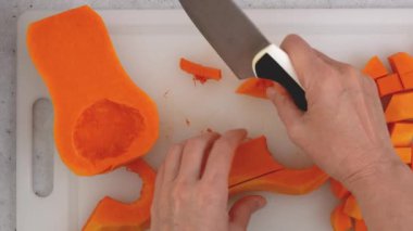 Tereyağlı kabak çorbası tarifi. Kadın balkabağı kesiyor. Mutfak masasının üzerinde çiğ sebzeler. Kabuğu soyulmuş ve çekirdeksiz kabak kesme tahtasına yakın çekim, düz yatış