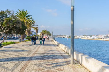 İnsanlar güneşli bir günün tadını çıkarırken Lagos rıhtımında gezinmek. Lagos, Portekiz, 30 Aralık 2024