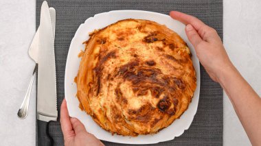 Şef taze pişmiş fileto hamurlu turtayı altın hamurlu sunar, dejenere olmuş krem peynir dolgusu sergilenir, düz uzanır.