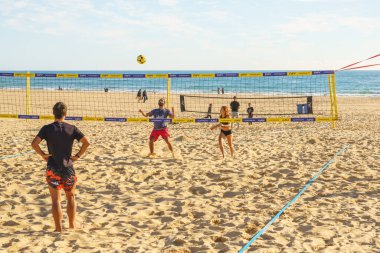 Portimao, Portekiz, 18 Ocak 2025. Güneşli bir günde plaj voleybolu oynayan insanlar ve arka planda kumlu sahil şeridi..