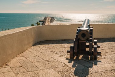 Marinaya, kumlu plaja ve açık mavi gökyüzünün altındaki kayalıklara bakan tarihi top..
