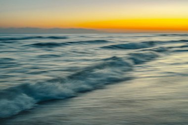 Gün batımının altın ve turuncu renklerini yansıtan bulanık okyanus dalgaları..