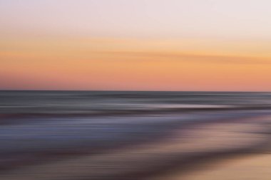 Yumuşak dalgalar ve pastel gökyüzü huzurlu ve soyut bir deniz manzarası yaratır..