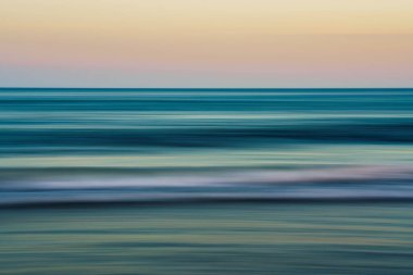 Bulanık okyanus dalgaları gün batımında pastel gökyüzü ile buluşur.