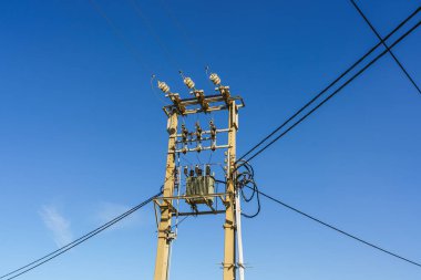 Yüksek voltajlı elektrik hatları ve trafolar mavi gökyüzünün altındaki elektrik direğinde..