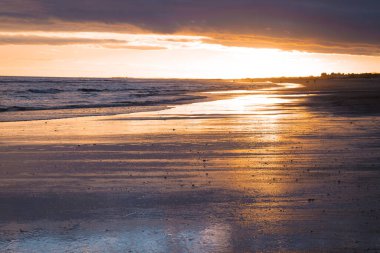 Altın güneş ışığı, sakin bir sahildeki ıslak kumlara yansıyor..