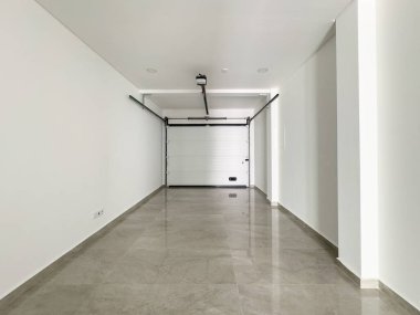 Temiz beyaz duvarları, motorlu kapısı ve geniş bir alanı olan minimalist bir garaj..
