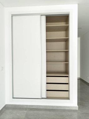 Beyaz sürgülü kapılı modern gardırop rafları ve çekmeceleri gözler önüne seriyor..