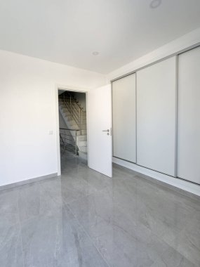 Modern minimalist oda, sürgülü kapı dolabı ve merdivene açılan açık beyaz bir kapı..