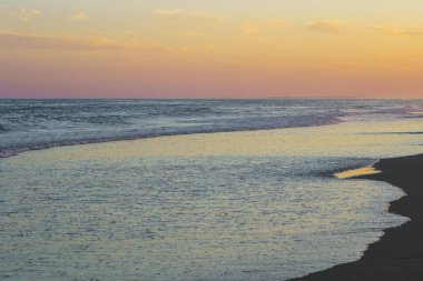 Akşam ışığı sahile vuran sakin okyanus dalgalarını yansıtıyor..