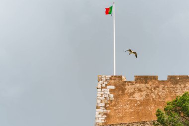 Eski bir kalenin yıpranmış taş duvarları Portekiz bayrağıyla dimdik ayakta duruyor..