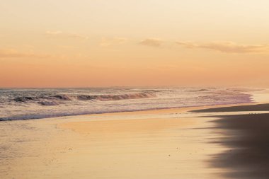 Altın gün batımı, dalgaların kumla nazikçe buluştuğu sakin kıyı şeridine yansıyor..